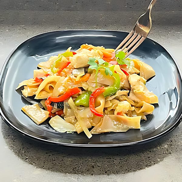 A fork lifts a bite of Thai noodles with chicken, red and green peppers, and cilantro.