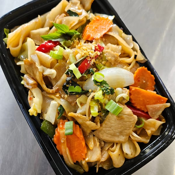 Close-up of Easy Thai Bend's Pad See Ew with wide noodles, chicken, and vegetables in a black container.