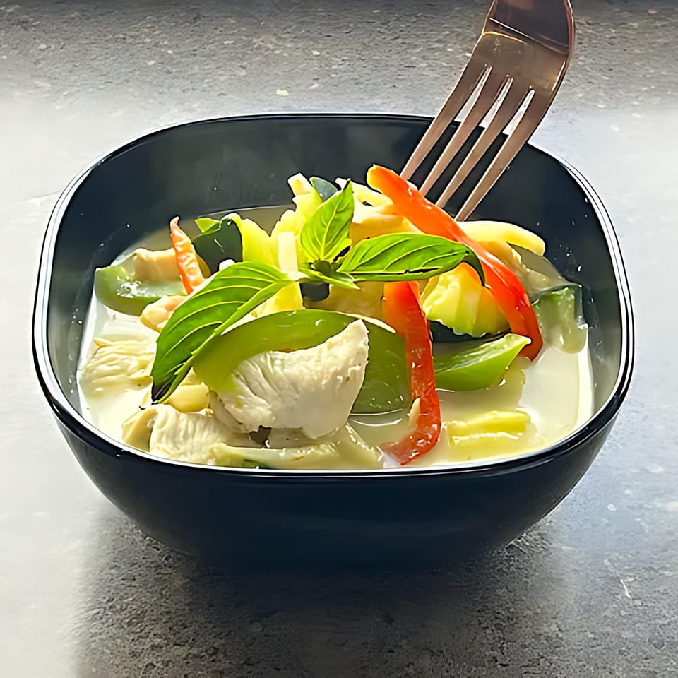 Easy Thai Bend's green curry with chicken, bell peppers, and basil in a black bowl.