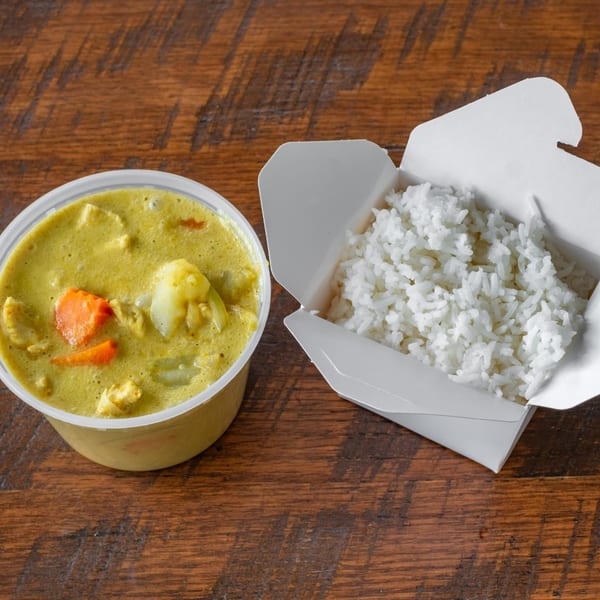 Easy Thai Bend yellow curry with chicken and vegetables in a plastic container next to white rice in a takeout box.