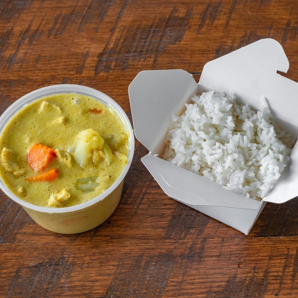 Easy Thai Bend yellow curry with chicken and vegetables in a plastic container next to white rice in a takeout box.