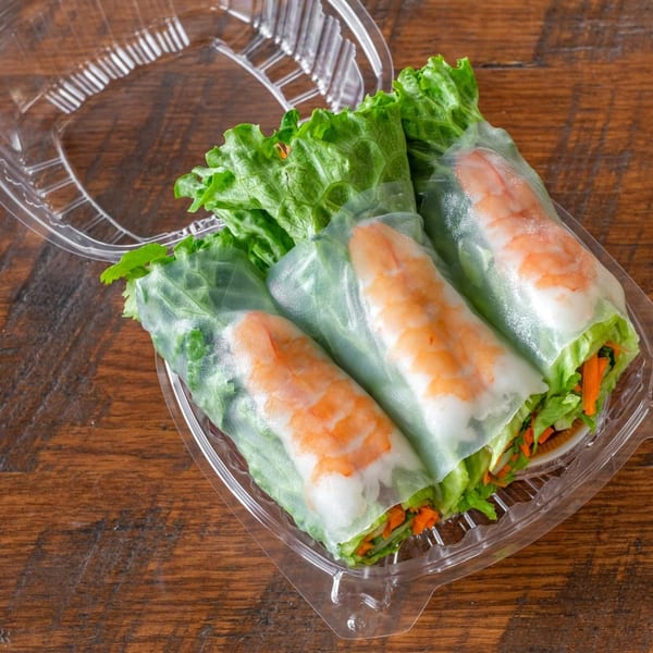 Three fresh shrimp spring rolls with lettuce and carrots in a clear plastic container.